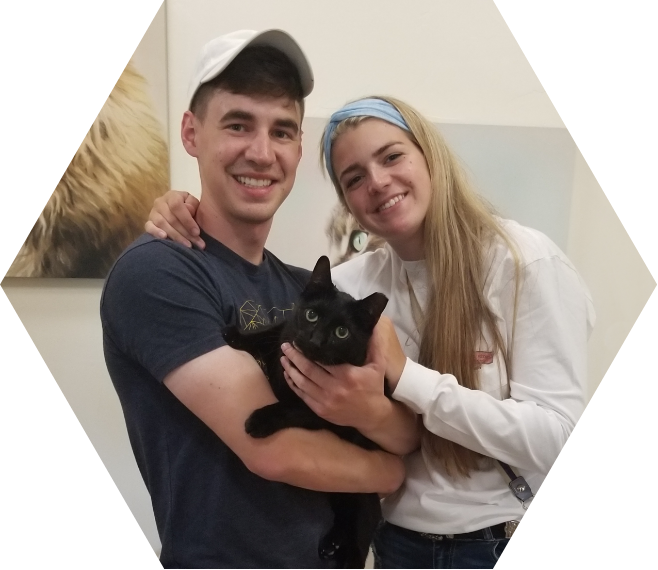 a male and a female cat shelter volunteer hold and pet a black cat